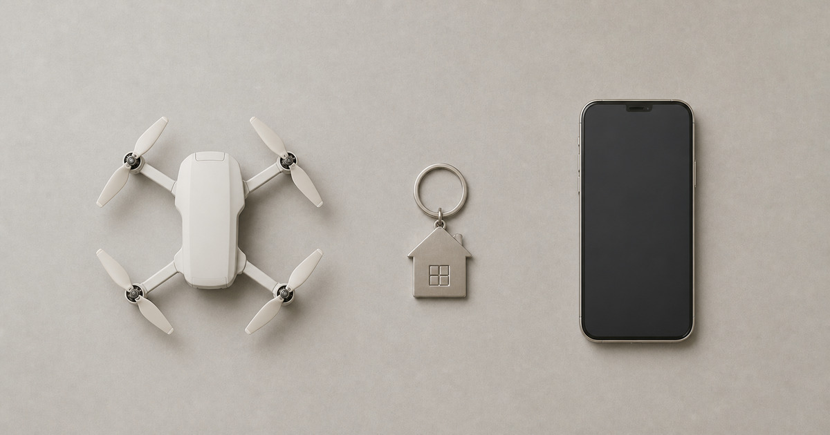 A camera drone and a smartphone on either side of a house-shaped keychain on a warm grey surface