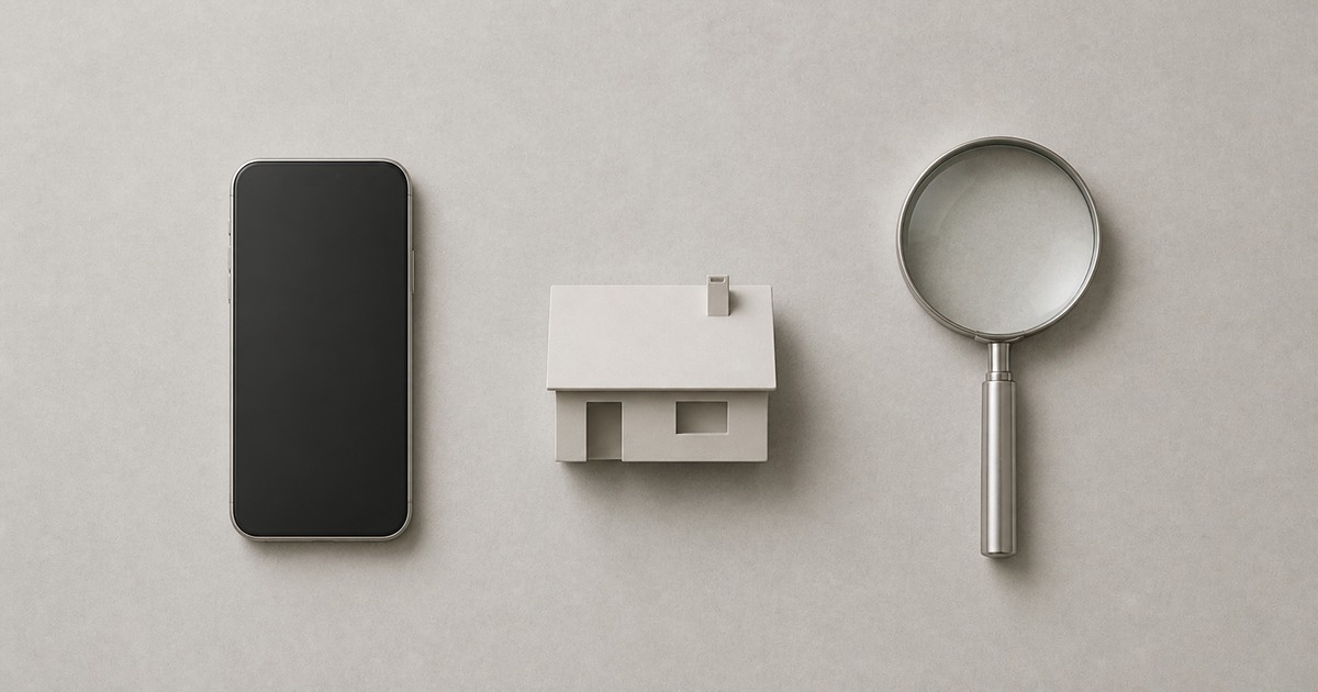 A smartphone, a small model house, and a magnifying glass on a warm grey surface
