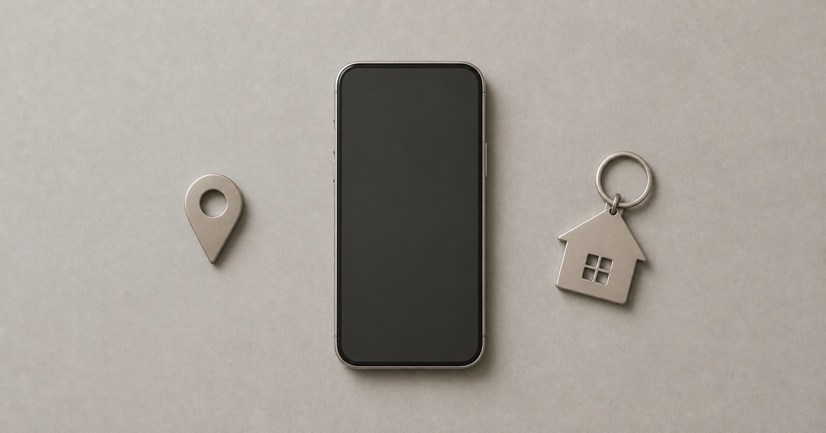 A smartphone, a metallic map location pin, and a house-shaped keychain on a warm grey surface